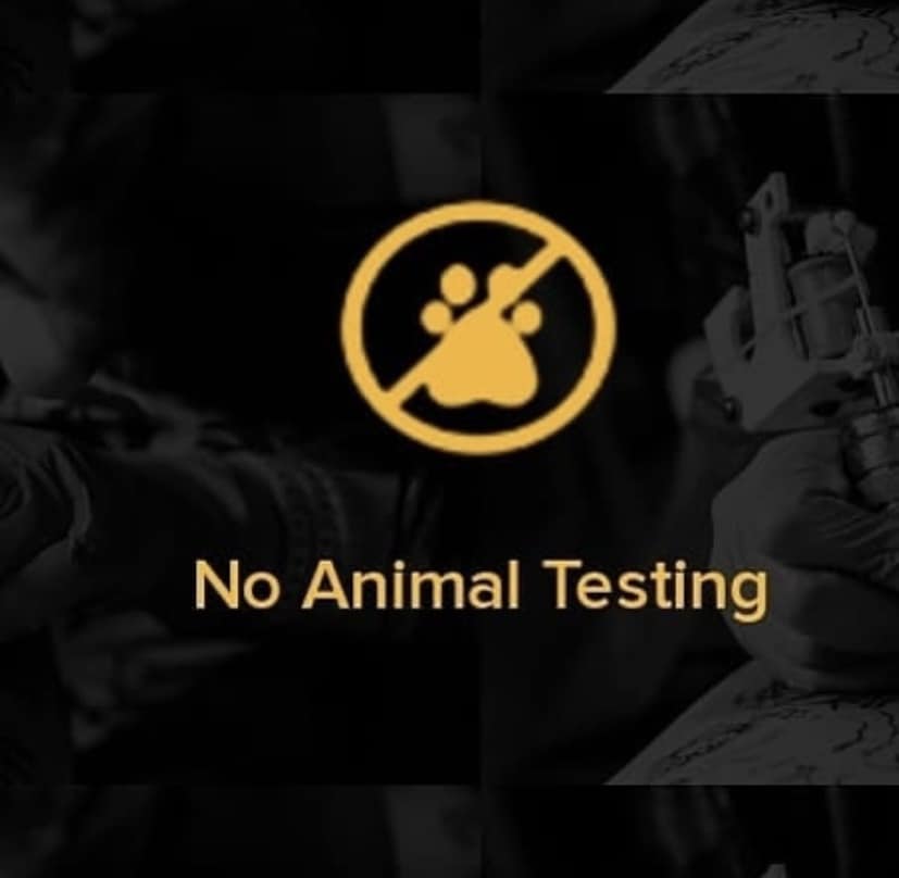 Black and white photo of a tattooist tattooing somebody, with yellow 'no animal testing' text on top and a paw print 'no' icon