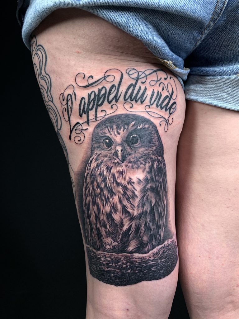 Black and white owl with lettering thigh tattoo on woman
