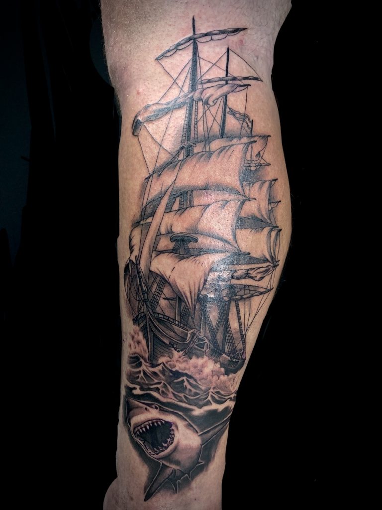 Black and white ship with great white shark leg tattoo on man