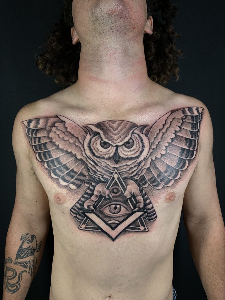 Black and white owl and illuminati chest tattoo on man