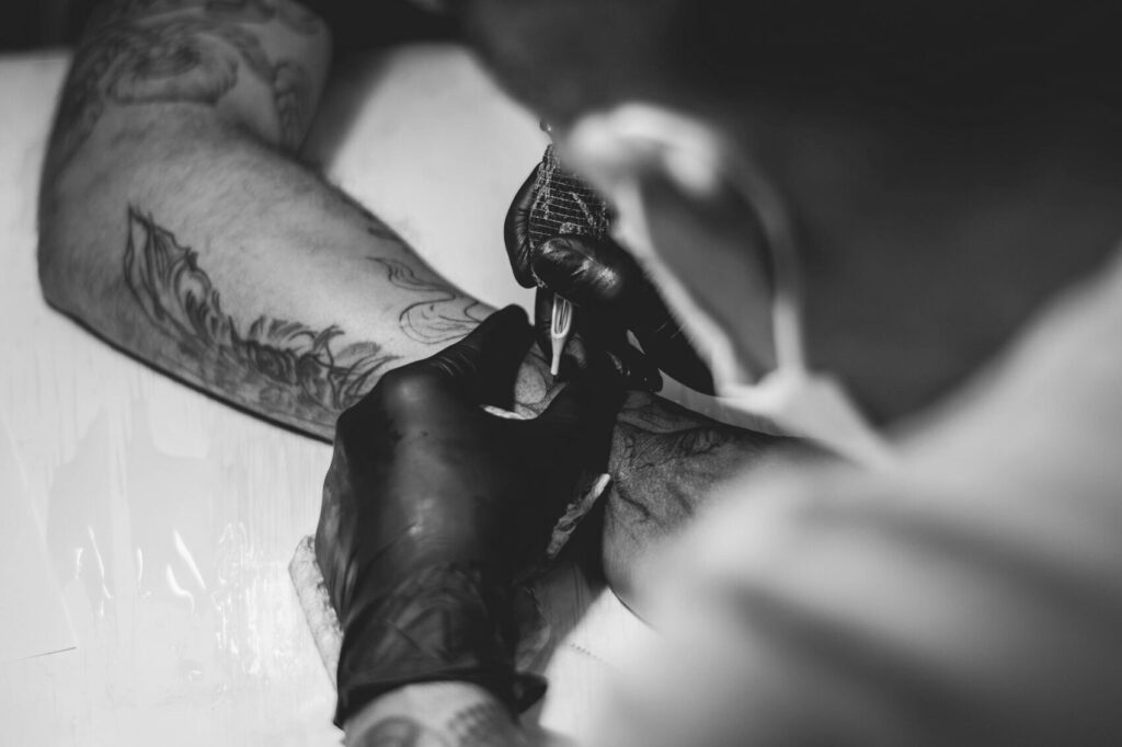 Black and white closeup of man tattooing an arm