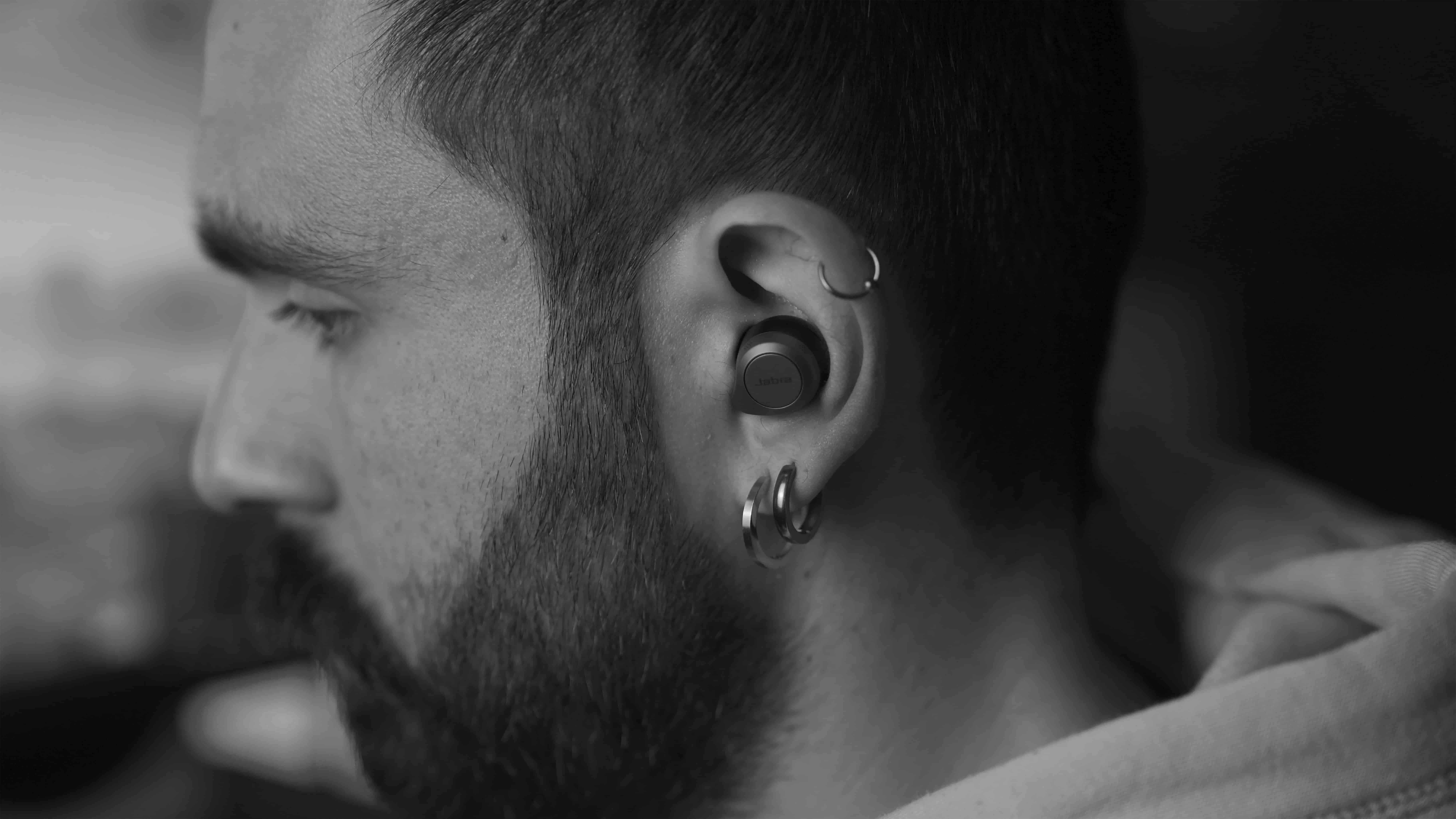 Closeup of the side of a man's face with ear piercings and wireless earbuds.